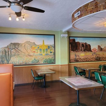 Char's Thai - the interior of a restaurant - The photo depicts the interior of a restaurant featuring desert-themed murals on the walls, including cacti and rock formations. The space has wooden flooring, green chairs around tables, and a ceiling fan with lights. A decorative ceiling feature with a patterned border and a chandelier is also visible. The overall setting suggests a casual dining environment. - Thai Near Me - Tucson, Arizona