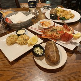 Crab Cake - A variety of seafood dishes such as crab, lobster, and fish are displayed on a wooden table, with sides and condiments, in a restaurant setting.