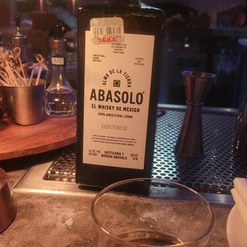 Bulevar Mexican Kitchen - A bottle of Abasolo whiskey and a glass of whiskey are placed on a bar counter with bar tools and bottles in the background. - Mexican Near Me - Austin, Texas