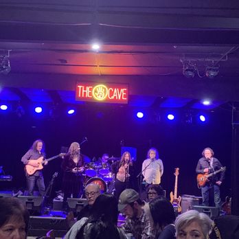 The Cave - a group of people on stage - A band performs live on stage at The Cave in Buffalo, NY, with multiple musicians playing instruments and singing, illuminated by stage lighting. - Music Venues Near Me - Buffalo, New York