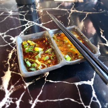 Zu Hot Pot - A ceramic divided dish containing two types of sauce with chopped green onions, placed on a black marble table with chopsticks resting on it. - Hot Pot Near Me - Albuquerque, New Mexico