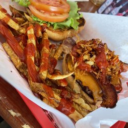 A burger with tomato slices, lettuce, and onion on a bun, accompanied by fries topped with ketchup and crispy fried onions.