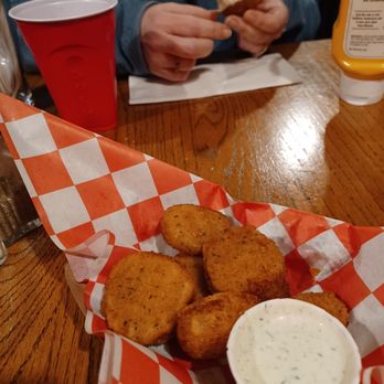 Layman Brewing - Deep fried pickles - Fried pickles served with a creamy dipping sauce are placed in a basket lined with red and white checkered paper at a dining table. - Brewpubs Near Me - West Allis, Wisconsin