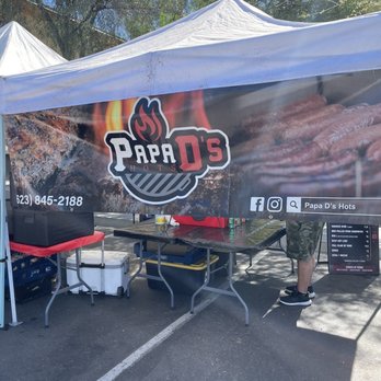 Pareja's Ace Hardware - Papa D'S BBQ smoker going today - A vendor tent for Papa D's Hots features a banner with images of grilled meats and the business logo, set up in an outdoor parking lot. - Hardware Stores Near Me - Phoenix, Arizona