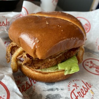 Slim Chickens - Cajun Ranch Chicken - A fried chicken sandwich features a crispy fried chicken patty, a leaf of lettuce, and a toasted bun. The sandwich is placed on branded paper with Freddy's logo, and a drink cup is visible in the background. The bun appears shiny and golden-brown, and the sandwich is presented in a typical fast-food setting. - Fast Food Near Me - Avon, Ohio
