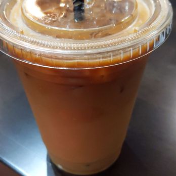Aquamos Coffee Collaborative - Yummmmmm - A clear plastic cup filled with iced coffee, topped with ice and a black straw, placed on a dark wooden table. - Coffee & Tea Near Me - Waupaca, Wisconsin