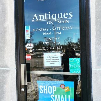 Antiques on Main - Enter here!! :) - The glass door shows the hours of operation for Antiques on Main, along with promotional stickers and signs, including a holiday season message. - Antiques Near Me - Crown Point, Indiana