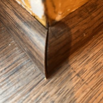Ed's Floor & Home - Sloppy .. - A detailed close-up of the junction between a wooden floor and a wooden furniture edge, showing the wood grain and joint. - Carpeting Near Me - Plaistow, New Hampshire