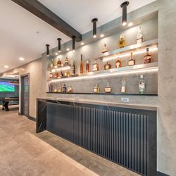 Basement Remodeling - Chic bar with backlit floating shelves, a modern black finish, and ample storage for spirits.