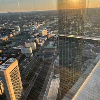 View Boston - Huntington Ave from above with a reflection of my foundation that rest below my feet, 51 floors above Boston. - A high-angle city view captured from a tall building, showing urban structures and streets, with a reflection of the setting sun on the glass window. - Observatories Near Me - Boston, Massachusetts