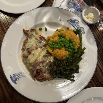 The Columbia - Pollo manchego - A plate featuring mashed yellow rice with peas, cooked greens, and a meat dish topped with melted cheese, served on a restaurant plate. - Spanish Near Me - St Augustine, Florida