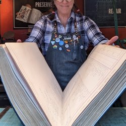 Owner Audra Loyal holding open a giant ledger that she repaired.