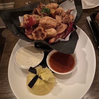 Mooo.... Beacon Hill - Crispy Calamari - Fried calamari served with two dipping sauces, one creamy and one red, on a white plate with a lemon wedge and a small wrapped item. - Steakhouses Near Me - Boston, Massachusetts