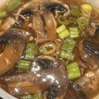 China Fun - Hot and Sour Soup - A bowl of hot and sour soup containing sliced mushrooms and chopped green onions in a dark broth. - Chinese Near Me - Austin, Texas