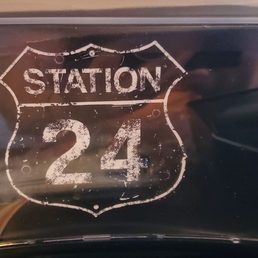 Logo - A sign displaying 'Station 24' in a distressed style, mounted inside a restaurant or diner setting.