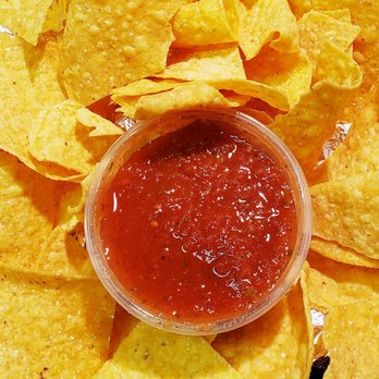 Bubbakoo's Burritos - Chips and Salsa For The WIN!! - A small clear plastic cup of red salsa is placed among yellow tortilla chips on a tray, with some chips overlapping the container. - Mexican Near Me - Mount Olive, New Jersey