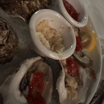 Pace's Steakhouse - App - A seafood platter featuring oysters with red and yellow sauces, along with condiments, on a white plate at a restaurant. - Steakhouses Near Me - Hauppauge, New York