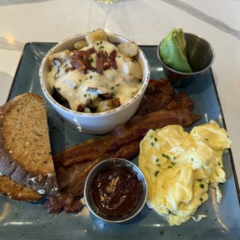 First Watch - Traditional Breakfast - A breakfast plate featuring scrambled eggs, crispy bacon, toasted bread, roasted potatoes, and a side of avocado in a small cup. - Breakfast & Brunch Near Me - Des Plaines, Illinois