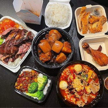 No 1 Express - a variety of asian food - The image shows multiple Chinese takeout dishes arranged on a black table. There is a container of white rice, a bowl of spicy soup with vegetables and meat, a dish with braised pork and vegetables, fried chicken pieces with dipping sauce, and a small container of sauce. The food is served in disposable containers, typical of takeout meals. - Chinese Near Me - Arcadia, California