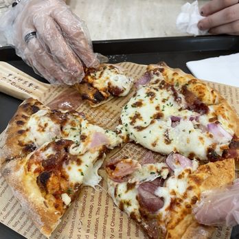 D T Restaurant - A person wearing a transparent glove is serving a slice of pizza with cheese, ham, and onions on a tray at a restaurant. - Pizza Near Me - Flushing, New York