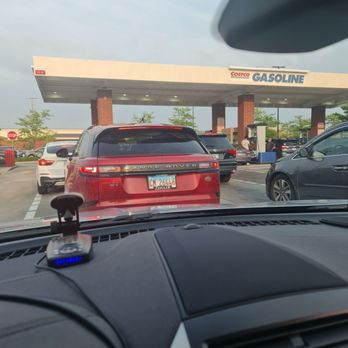 Costco Gasoline - Inside a car, looking out at a Costco Gasoline station with parked cars and a gas station canopy. - Gas Stations Near Me - Schaumburg, Illinois