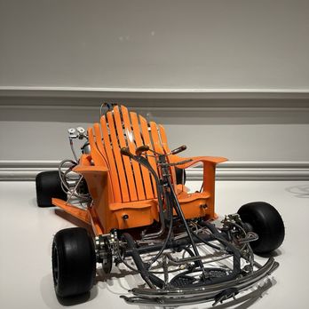 Renwick Gallery - A vehicle with a bright orange bench seat, large tires, and exposed mechanical components is displayed in a gallery setting. - Art Galleries Near Me - Washington, DC, District of Columbia