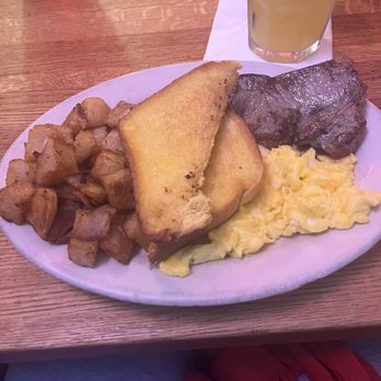 Texaz Grill - Steak and eggs - A breakfast plate includes diced potatoes, two slices of toasted bread, scrambled eggs, a piece of steak, and a glass of lemonade on a wooden table. - Steakhouses Near Me - Phoenix, Arizona