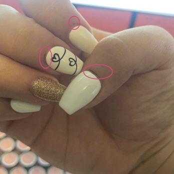 Nail's Corner - The image features a close-up of a hand with manicured nails, including a gold glitter nail and a white nail with black line art. Pink circles highlight small imperfections or marks on the nails and skin, such as scratches or blemishes. The background is blurred, focusing on the hand and nails. - Nail Technicians Near Me - Keizer, Oregon