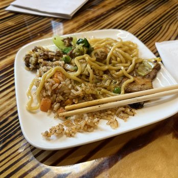 Bao - Ramen noodles - A white plate holds leftover Asian cuisine, including noodles, fried rice with vegetables, and a piece of meat, on a wooden table. - Asian Fusion Near Me - Pittsburgh, Pennsylvania