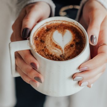 Sonder - a woman holding a cup of coffee with a heart on it - Coffee & Tea Near Me - Vancouver, British Columbia