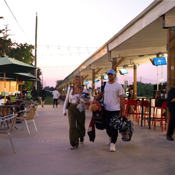 iRange Toronto - Two golfers walking with golf bags, in a path between the bays and the patio. 
You can always bring your own clubs or rent our clubs ! - Golf Near Me - Brampton, Ontario