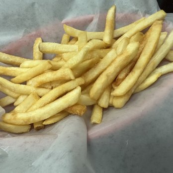 George's Gyros - A serving of French fries is shown on parchment paper, with a mix of light and slightly darker fries. The fries are cut into thin strips and appear crispy. The background includes a dark surface and a piece of foil or aluminum wrap on the side. - American Near Me - Chicago, Illinois