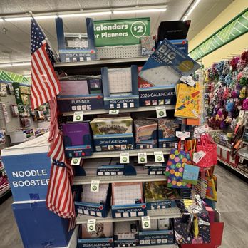 Dollar Tree - Shelf with 2026 calendars and planners, including various styles and sizes, in a retail store. An American flag is attached to the side of the display. - Discount Store Near Me - Cedar Park, Texas