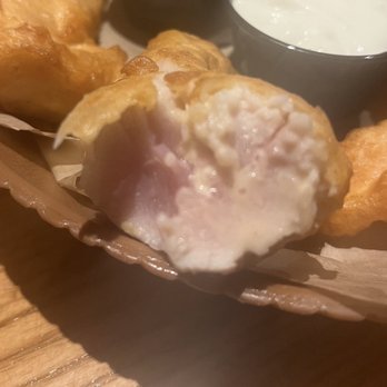 Chili's - The image shows a fried cheese ball with a golden-brown exterior and a soft, melted cheese interior. It is placed on a paper-lined basket, with a small container of white dipping sauce, likely ranch or sour cream, visible in the background. The setting appears to be a casual dining environment, possibly at a restaurant or bar offering appetizers. - Bars Near Me - Lone Tree, Colorado