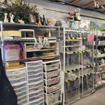 Lively Mind Art Studio - Metal shelving units contain ceramics, decorative objects, and art supplies, with some items covered in plastic, in an art studio setting. - Arts & Crafts Near Me - Phoenix, Arizona