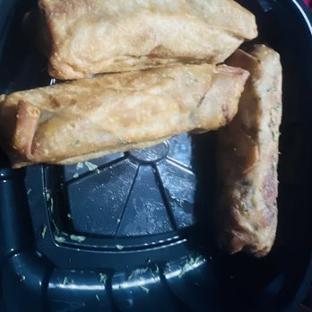 Oooh We It Is - Salmon egg rolls . - Three fried egg rolls or spring rolls with a golden-brown, crispy exterior are arranged on a black tray. The rolls appear to be freshly cooked, with some green herbs visible on the surface. The tray has some residual oil and small bits of food, indicating recent preparation or serving. - American Near Me - Chicago, Illinois
