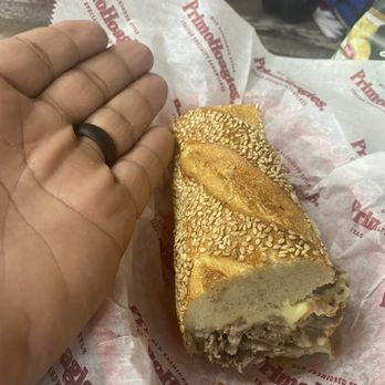 PrimoHoagies - A sandwich with a sesame seed bun and meat filling is placed on branded paper from PrimoHoagies, with a hand nearby. - Sandwiches Near Me - Wayne, New Jersey