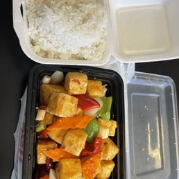 General Tsao's Tofu with rice - A takeout meal includes a container of white rice, a tofu stir-fry with vegetables, and a separate empty container for sauce.