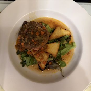 Le Central - Osso buço - A dish with a meatloaf topped with diced vegetables, accompanied by toasted bread triangles and mixed greens, served on a white plate. - French Near Me - Bristol, Rhode Island