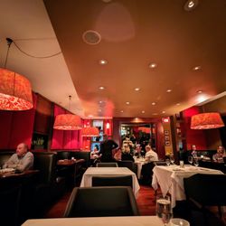 Bin 54 Steak & Cellar - Inside. Dining room. Wide U-shaped booth seating along the perimeter of the main dining room. White tablecloth smaller tables in the center.