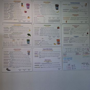 Smoothie World - Menu - Six printed menu posters are affixed to a white interior wall, each listing various smoothie flavors, ingredients, and prices. The posters include colorful images of smoothies and are arranged in two rows of three. To the right, a handwritten sign advertises ice cream flavors and prices. The ceiling has a fluorescent light panel, and the floor is tiled with light-colored tiles. - Pop-Up Restaurants Near Me - Bear, Delaware