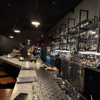 Nightcap - Bar - A bar interior featuring a marble countertop, shelves stocked with various liquor bottles, and bartenders preparing drinks in a dimly lit setting. - Cocktail Bars Near Me - Ann Arbor, Michigan