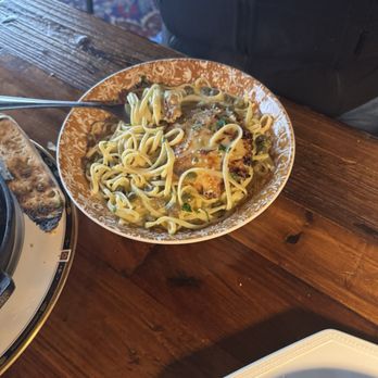 Kitchen and Rail - Lemon piccata - A bowl of lemon piccata pasta with sauce and herbs is placed on a wooden table in a restaurant setting. - Bars Near Me - Eagan, Minnesota
