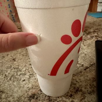 Chick-fil-A - A large foam cup featuring the Chick-fil-A logo in red is held by a person's hand with neatly manicured nails. The cup is placed on a speckled granite countertop, with a blurred background indicating a kitchen setting. The cup appears to be filled with a beverage, and the foam material suggests it is designed for hot or cold drinks. - Fast Food Near Me - Mattoon, Illinois