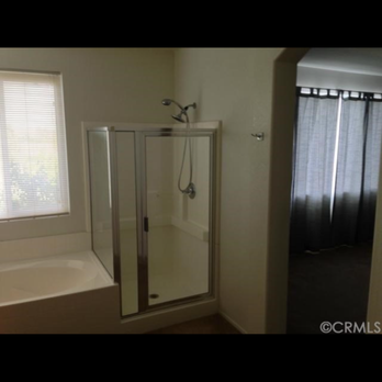 Cova Construction - Old before pic of master - A bathroom features a bathtub and a separate glass shower enclosure, with a window on the left and a doorway with curtains on the right. - General Contractors Near Me - Corona, California