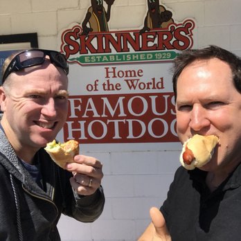 Skinners - two men eating hot dogs in front of a sign - Fast Food Near Me - Lockport, Manitoba Skinners - two men eating hot dogs in front of a sign - Fast Food Near Me - Lockport, Manitoba