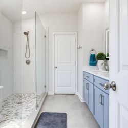 Gill Construction - Primary bathroom remodel with a mist-blue double vanity, a frameless glass walk-in shower and a river-pebble floor.