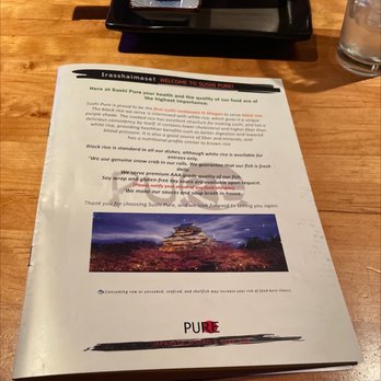 Sushi Pure - A printed menu from Sushi Pure, a Japanese restaurant, is placed on a wooden table, with a glass of water and black tray in the background. - Sushi Bars Near Me - Eugene, Oregon