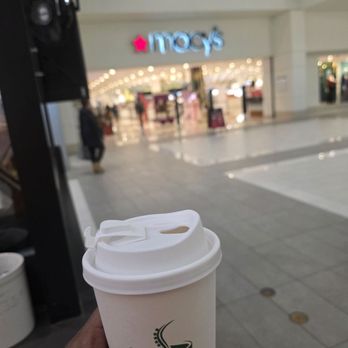 Cath Coffee - A person holds a coffee cup from Cath Coffee in front of a Macy's store inside a shopping mall. - Coffee & Tea Near Me - Indianapolis, Indiana