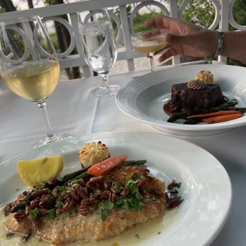 Blu - Blu absolutely amazing. A beautiful view on the patio and exquisite along with wonderful service. We went for our 10 year anniversary - A lakeside restaurant table set with two plates of gourmet dishes, two glasses of white wine, and a water glass, with a view of trees and water in the background. - French Near Me - Glen Arbor, Michigan